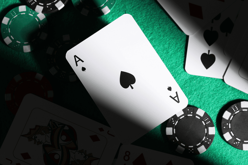 Ace of spades playing card prominently displayed on green casino felt surrounded by black and white chips – baccarat card values and natural hand rules